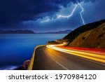 The lights of vehicles on the coastal road at night are getting longer. Lightning falling from the sky to the sea creates a perfect view with the vehicles moving fast on the highway.
