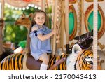 Adorable little girl in blue dress at amusement park having a ride on the merry-go-round