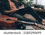 Small photo of young man relax and playing guitar while sitting on sofa bed in living room at home. Music create melody song, lyrics on laptop and practice concept.