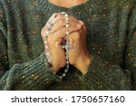 Close up of a woman with prayer hands folded to the chest holding a Rosary beads. Building deeper relationship with through praying The Rosary everyday concept.