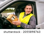 Small photo of Postman in car. Postman driving van. Mail worker with cardboard box. Deliveryman smiles and looks into camera. Courier service driver. Deliveryman portrait at work. Delivers orders. Postman career