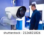 Small photo of White CCTV camera in store. Sale of video surveillance systems. White IP camera close-up. Concept - complex video surveillance systems. Selling IP video surveillance systems. Blurred man in background