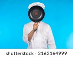 Small photo of Chef cook covers his face with frying pan. Restaurant chef on turquoise background. Kitchen utensils in man hand. Concept - kitchen utensils for cooking food. Selling kitchen utensils for restaurant