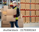 Small photo of Bonded warehouse. Woman customs officer. Concept checking cargo at state border. Customs officer with boxes. Woman in protective helmet carries parcels. Distribution warehouse. Work at customs