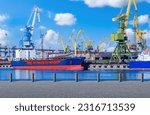 Small photo of Seaport in sunny weather. Ships in process of unloading. Cranes in harbor. Equipment for unloading ships. Seaport on summer day. Ship transportation of goods. Empty jetty in seaport.