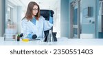 Small photo of Woman biologist. Girl student in laboratory. Biologist is holding test tube while sitting at table. Laboratory technician makes notes in clipboard. Biologist woman conducts scientific experiments