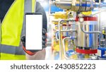 Small photo of Mobile phone in hands of industrialist. Factory worker holds smartphone. Phone with blank screen. Cellphone near industrial equipment. Person in reflective vest recommends apps. Industrial mock up
