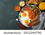 Full English breakfast on a plate with fried eggs, sausages, bacon, beans, toasts and coffee on dark stone background. With copy space. Top view.