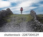 Young teenager girl walking up a hill on a rough small country road between stone fences. Aran Island, Ireland. Travel and tourism concept. Explore stunning Irish nature concept.