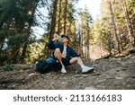 Small photo of A male tourist in casual clothes sits in the mountains on a trail and sat down to rest, drinking water from a bottle and looking away. Hiker at a halt while climbing a mountain.