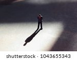Lone man in empty space with dramatic shadow. Looking down at feet, he has a look of guilt or shame. Businessman guilty of white collar crime or dishonesty. Silhouette of unrecognizable shadow man. 