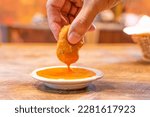 Small photo of Hand holding a chicken nugget and dipping in spicy chili sauce