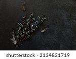 Happy Easter concept. Preparation for holiday. Pussy willow flowers branches, feather on trendy grunge scratched dark black stone shale background. Simple minimalism flat lay top view copy space