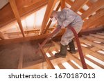 Worker with a hose is spraying ecowool insulation in the attic of a house. Insulation of the attic or floor in the house