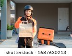 Delivery Asian man wearing orange uniform and ready to send delivering Food bag in front of customer houes with food case box on scooter, express food delivery and shopping online concept.