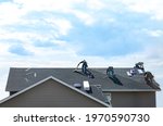 4 construction workers fixing roof against clouds blue sky. Roofer install shingles at the top of the house. Renovate, improve, build home exterior by professional teamwork. Safety, protection concept