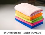 Small photo of stacked colorful microfiber cleaning cloths on a pink background. Colorful, dry microfiber cloths for different surfaces cleaning in kitchen, bathroom ,other rooms. Copy space for text or logo.