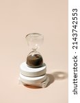 Small photo of A side view of an hourglass with elapsed time sand, on a beige background with hard shadow copy space, concept of transience of time, expired deadlines for work