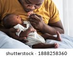 An African American father kissing hand,  his 12-day-old baby newborn son lying in bed in a white bedroom, with happy, concept to African American family and newborn