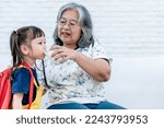 Small photo of Blurred soft images, an elderly Asian grandmother is holding a glass of milk for her granddaughter to dirk before going to school in the morning, to children health care and back to school concept.