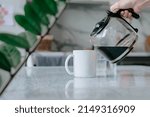 Woman's hand pours freshly brewed coffee into a mug for breakfast.