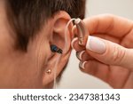 Small photo of A woman tries on a hearing aid hidden in her ear on a light background. Restoration of hearing. Technical means