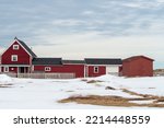 Small photo of A red farm house with multiple additions and outcrop buildings with a grassy meadow in the foreground. It's winter with white snow on the ground. The buildings have black roofs, and white windows.