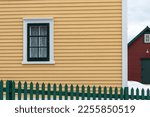 A bright and cheerful yellow country house with wood cape cod clapboard, white trim, and multiple windows. There's a green wooden picket fence in the front of the building enclosing the garden.