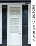 Small photo of A navy blue wooden house wall with a half glass four pane window in the panel exterior door. There's a metal doorhandle, transom window with white curtains. The doorway entrance is to a country house.