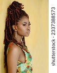 Small photo of Close-up profile photo of the magnificent young black woman with long eyelashes, wearing a bright multicolor dress and eloquent earrings, looking away, isolated on a yellow wall background.
