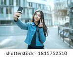 Teenager girl in urban city take selfie picture by smartphone in public with fingers symbolize peace and mouth shaped as kissing duck face for followers at social media