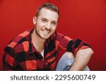 Small photo of nonchalant guy sit with elbow to knee and arm on his leg while look at camera at smile happy with red flannel shirt look like a joyful handyman