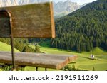 (Selective focus) Defocused park bench in the foreground with the Church of St. John (San Giovanni in Ranui) that stands out in the green meadows, in the heart of the beautiful Dolomitic landscape.	