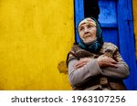 Small photo of The old grandmother in the background of the slums. An elderly woman in a poor area. Grandmother on a yellow background. Poverty and disadvantage concept. Helping vulnerable populations