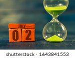 Small photo of july 2nd. Day 2 of month,Handmade wood cube with date month and day and hourglass with green sand. Time passing away. artistic coloring. summer month, day of the year concept