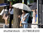 Small photo of Young Japanese woman protecting herself from the sun with an umbrella in Tokyo on a hot summer day.