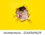 Small photo of Close-up of a man's ear and two hands through a torn hole in the paper. Yellow background, copy space. The concept of eavesdropping, espionage, gossip and tabloids.