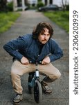 Small photo of An adult underdeveloped crazy man, an idiot, an imbecile rides a children's small bicycle in a park on the road. Photography, mental illness.