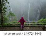 Small photo of Moslem woman enjoying Tumpak Sewu waterfall which located at Lumajang, East Java, Indonesia even the weather is unpredicted and become foggy, she still can