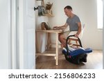 Small photo of A handsome freelance man works on a modern laptop. A young father works at home and cradles his little son in a cradle. High quality photo