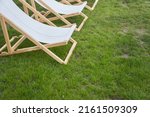Small photo of Part of a lightweight folding chair for outdoor recreation. An empty white wooden chaise longue on the green grass of a fresh lawn with a place to copy. High quality photo