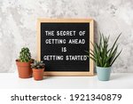 The Secret Of Getting Ahead Is Getting Started. Motivational quote on letter board, cactus, succulent flower on white table. Concept inspirational quote of the day. Front view.