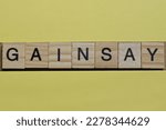 Small photo of the word gainsay of gray small wooden letters lies on a yellow table