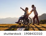 Disabled handicapped young man in wheelchair walking with his care helper in sunset.Silhouette