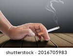 Small photo of Cigarette in male hand on desk.Concept of chain smoker.