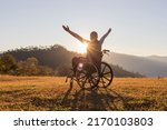 Person sitting on a wheelchair enjoying sundown on mountain background.