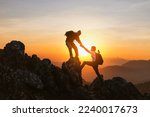 Small photo of Silhouette Two Male hikers climbing up mountain cliff and one of them giving helping hand. People helping and, team work concept.
