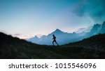 A single trail runner, silhouetted against the sky at sunrise while running in the mountains of the Alps along a steep trail