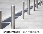 Diagonal row of chrome metal bollard poles along a concrete sidewalk, with space for text on the right