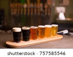Small photo of Close up of craft beer tasting flight at local brewery of small pint glasses in a row on a tray with rainbow variety of dark malt stouts to golden yellow hoppy ales on bar, with taps in background